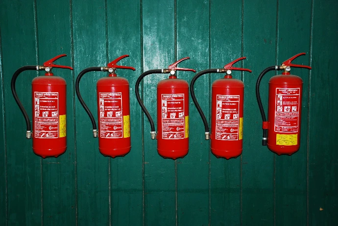 four fire extinguishers lined up against a green wall